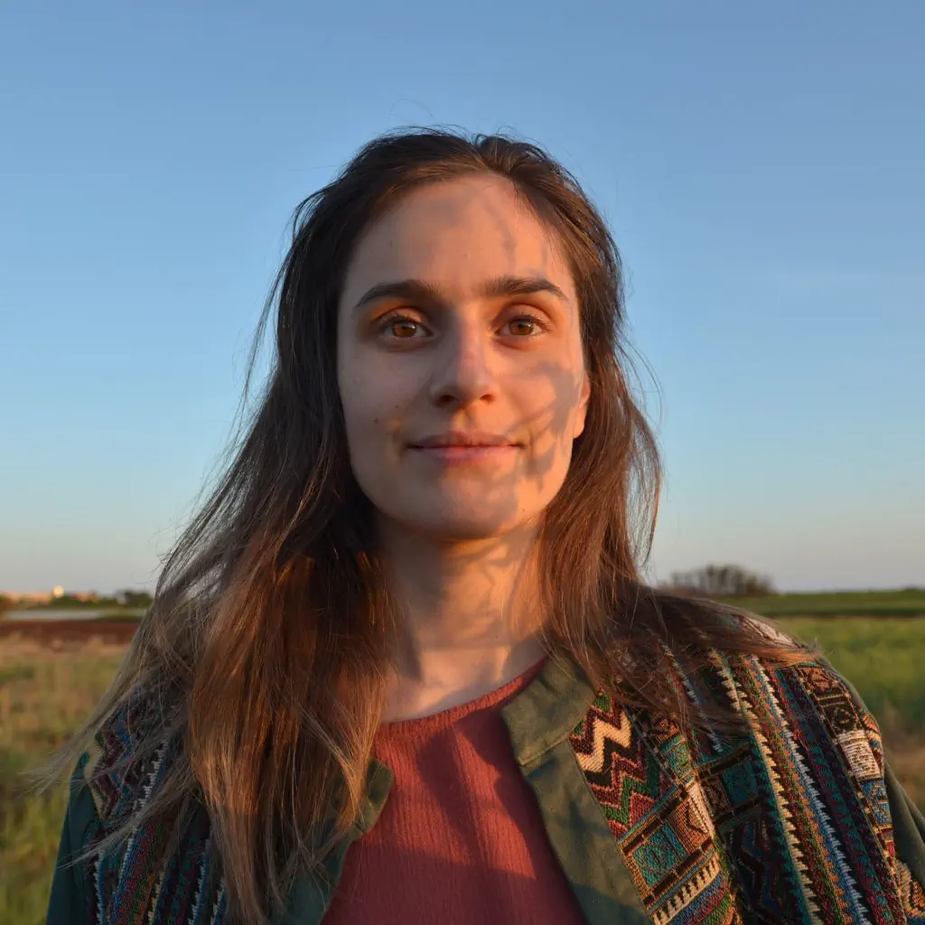 Photograph of Anastasiia Artiukhina against a natural Mediterranean scrub background at sunset, with shadows of wildflowers decorating one side of her face